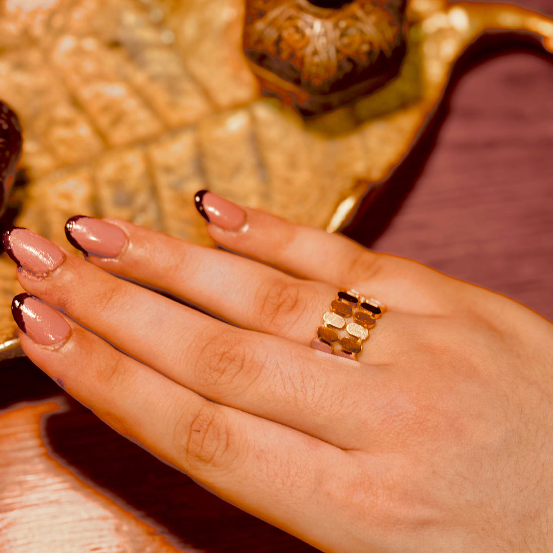 Hand wearing a gold ring on a decorative surface